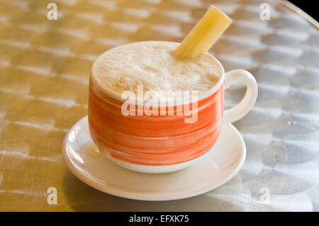 Vista orizzontale di un cappuccino caffè servito con un pezzo di canna da zucchero in esso, Cuba. Foto Stock