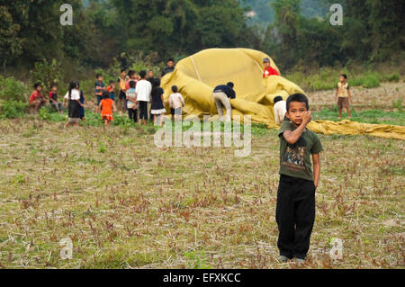 Vista orizzontale di giovani laotiani bambini aiutando a riporre una mongolfiera sbarcati vicino al loro villaggio. Foto Stock