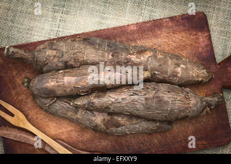 Un mucchio di manioca (Lat. Manihot esculenta) sulla tavola di legno fotografati con luce naturale (messa a fuoco selettiva) Foto Stock