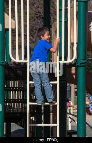 Popolazione ispanica giovane ragazzo a riprodurre la scaletta di arrampicata sul parco giochi in Pioneer Park nella città di Novato California Foto Stock