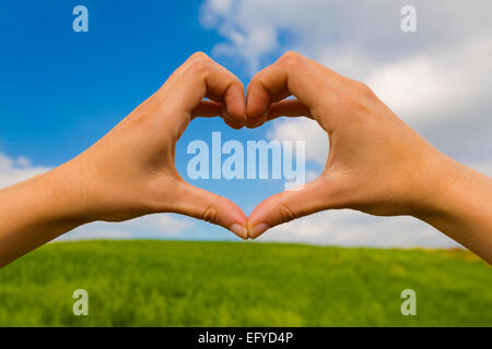 Femmina facendo a mano a forma di cuore contro un bel cielo azzurro Foto Stock