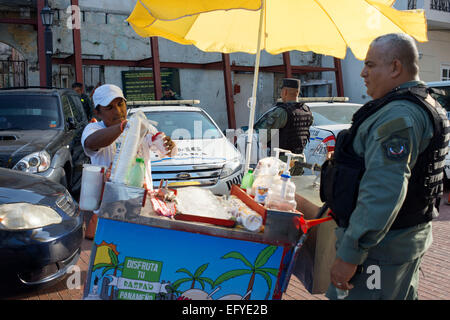 PANAMA CITY, PANAMA - Venditore per la vendita di frutta aromatizzate con ghiaccio e rasata, noto come raspado al soldato dell'esercito di polizia. Radere il ghiaccio è a l Foto Stock