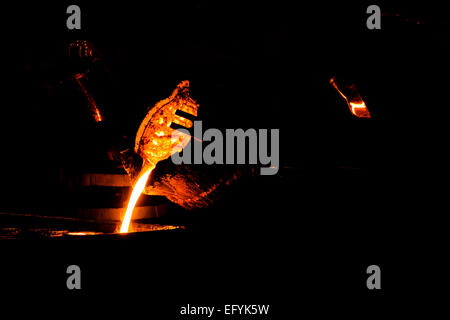 Lavoratori fonderia di versare il metallo fuso da un forno utilizzando un crogiolo in calchi di sabbia Foto Stock