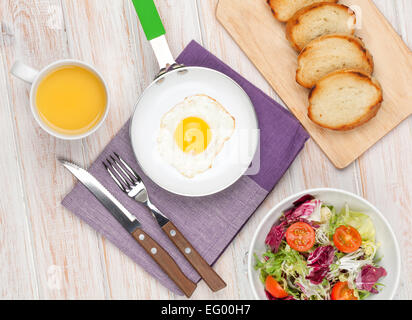 Sana colazione con uovo fritto, toast e insalata su bianco tavolo in legno Foto Stock