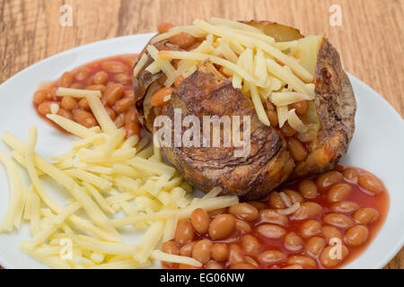 Un caldo cotto jacket potato piena di formaggio grattugiato e fagioli al forno - studio shot Foto Stock