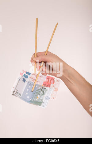 Mano femmina con bacchette e le banconote in euro Foto Stock