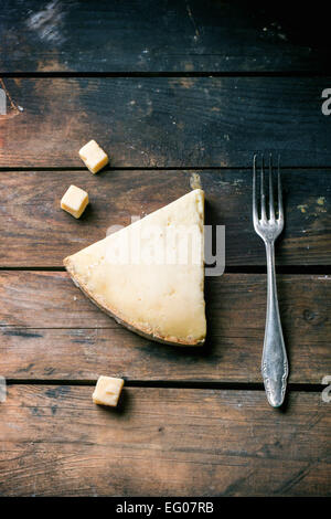 Pezzo grosso e cubetti di formaggio belga con forcella vintage su sfondo di legno. Vista dall'alto. Foto Stock