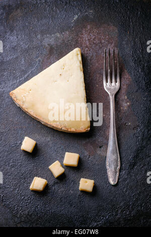 Pezzo grosso e cubetti di formaggio belga con forcella vintage su sfondo nero. Vista dall'alto. Foto Stock