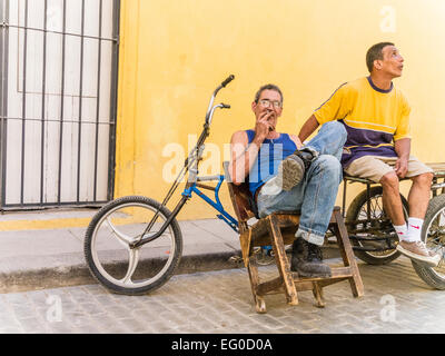 Due consegna biciclette uomini seduti a loro 3 ruote di biciclette di consegna contro una parete gialla e parlare a l Avana Vieja, Cuba. Foto Stock