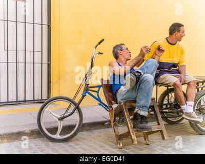 Due consegna biciclette uomini seduti a loro 3 ruote di biciclette di consegna contro una parete gialla e parlare a l Avana Vieja, Cuba. Foto Stock