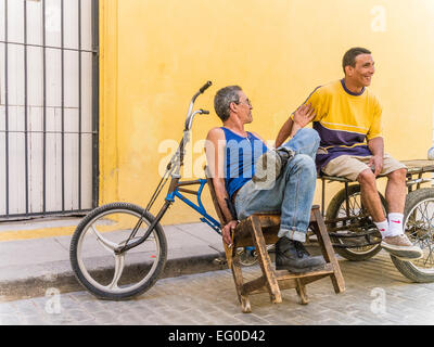 Due consegna biciclette uomini seduti a loro 3 ruote di biciclette di consegna contro una parete gialla e parlare a l Avana Vieja, Cuba. Foto Stock