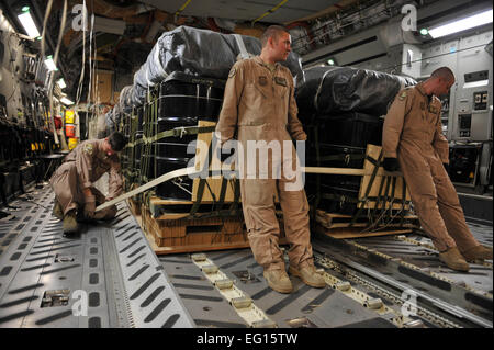 Stati Uniti Air Force loadmaster Senior Airman Josh Faust, sinistra, fascette contenitore sistema di consegna fasci per il pavimento di un C-17 Globemaster III, mentre il personale loadmaster Sgt. Gabriel risme, centro, e pilota Capt. Dave Goodale tenere i fasci in luogo a Kandahar Airfield, Afghanistan, 27 maggio 2010. L'equipaggio liberato i fasci oltre l'Afghanistan, il rifornimento della Combined Joint Special Operations Task Force con cibo e acqua e carburante. Capitano Goodale, sergente risme e Airman Faust sono assegnati alla 816th Airlift Expeditionary Squadron. Il personale Sgt. Quinton Russ Foto Stock