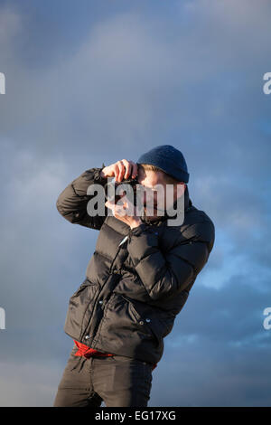 Giovane uomo che indossa 'puffa' giacca e cappello di lana in inverno scattare una fotografia con una fotocamera da 35mm. Foto Stock