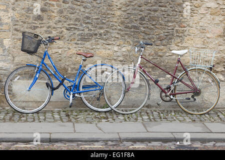 Due biciclette appoggiato uno sbriciolamento muro di mattoni su una mattonella pavimentazione di pietra a Oxford Foto Stock