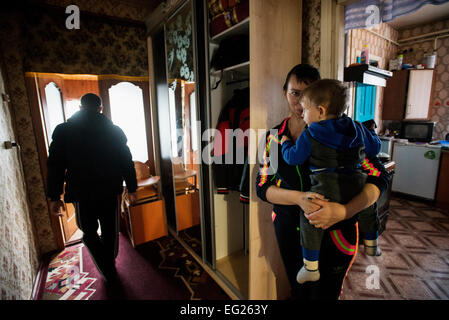 ATO il soldato Blyzniuk Ruslan, licenziato dopo che egli è stato ferito in quattro posti presso la sua gamba destra, va fuori la casa mentre sua moglie tenendo il loro figlio Artem, Radomyshl district, Ucraina Foto Stock