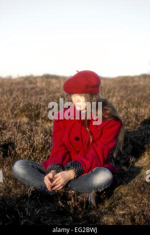 Una ragazza in un rivestimento di colore rosso è seduta su una collina Foto Stock