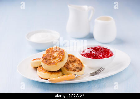 Cottage cheese pancake con confettura di ribes e panna acida, luce sfondo blu, il fuoco selettivo Foto Stock