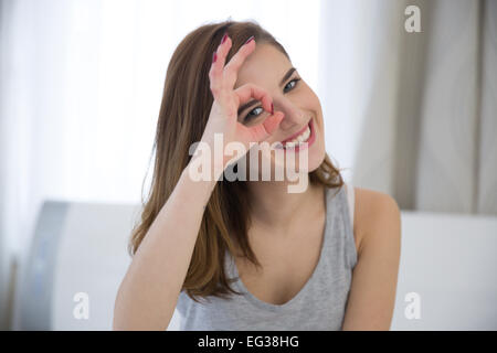 Donna felice guardando attraverso le dita a casa Foto Stock