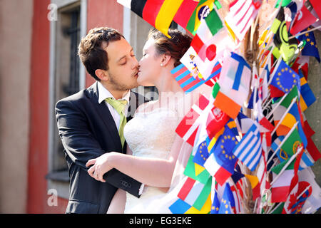 Coppia giovane dopo il matrimonio baciare in un abbraccio sulle bandiere internazionali sullo sfondo Foto Stock