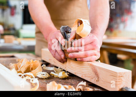 Carpenter lavora con una Pialla per legno sul pezzo in lavorazione nella sua officina di carpenteria o Foto Stock
