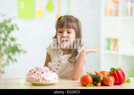 Kid scegliendo tra ortaggi sani e gustosi cake Foto Stock