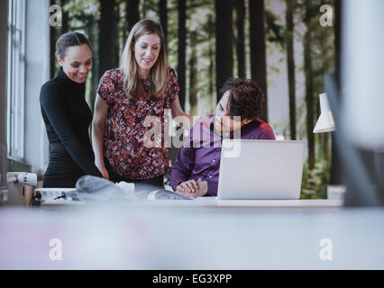 Team di giovani professionisti in cerca di un catalogo e sorridente. Il team creativo insieme la visualizzazione a un libro sulla scrivania. Foto Stock