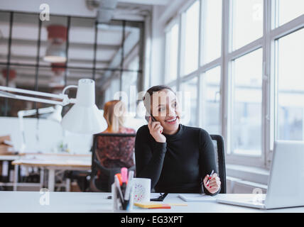 Giovane donna africana utilizzando il telefono cellulare mentre si è al lavoro. Executive femmina in conversazione su un telefono cellulare durante la seduta. Foto Stock