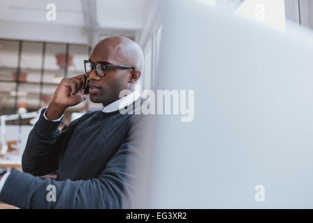 Colpo di un giovane imprenditore parlando al cellulare mentre si è al lavoro. Bald african executive in una conversazione con il cliente sul mobile pho Foto Stock