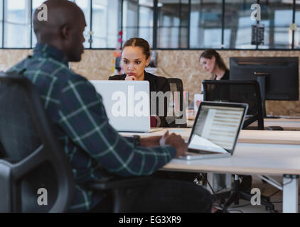 Giovane donna africana seduto alla sua scrivania che lavora sul computer portatile. Imprenditrice guardando lo schermo del notebook. Foto Stock