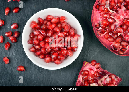 Rosso i semi di melograno in una ciotola bianco sul tavolo. Aprire freschi maturi melograno. Foto Stock