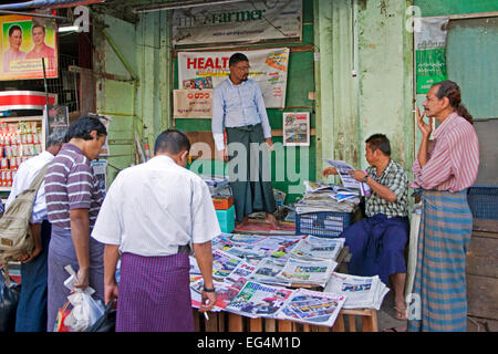 Gli uomini birmani acquisto di quotidiani e riviste in stallo di strada in Yangon / Rangoon, ex capitale del Myanmar / Birmania Foto Stock