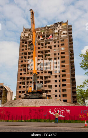 Una demolizione gru si siede di fronte a un parzialmente demolito a torre a Ibrox, vicino Govan nel sud ovest di Glasgow. Foto Stock