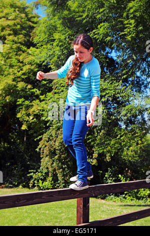 Giovane ragazza irlandese tightrope passeggiate su una staccionata di legno nel suo giardino in Irlanda rurale Foto Stock