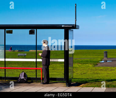 Giovane uomo in tuta in attesa ad una fermata degli autobus con il mare dietro a Whitley Bay North Tyneside Tyne and Wear England Regno Unito Foto Stock