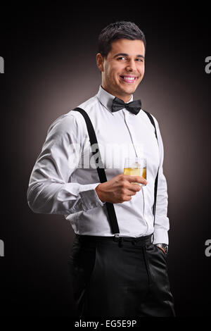 Colpo verticale di un allegro uomo beve bourbon su sfondo nero Foto Stock