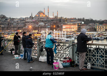 ISTANBUL, Turchia / Türkiye - i pescatori fiancheggiano il bordo del ponte di Galata con le loro linee sul lato del Corno d'Oro. Attraversando il Corno d'Oro e collegando Eminonu con Karakoy, il ponte Galata è un ponte a due livelli che gestisce il traffico stradale, del tram e pedonale al piano superiore con ristoranti e bar al livello sottostante. In lontananza c'è la Moschea Suleymaniye. Foto Stock