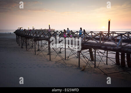 I turisti a piedi il molo in legno a Pimentel beach nel nord del Perù in serata luce arancione del tramonto Foto Stock