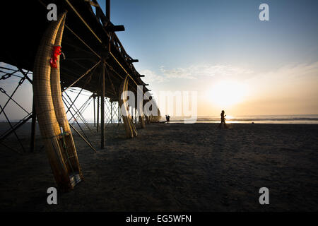 Caballitos de Totora (reed tradizionali canoe pesca) e gente che cammina nel sole di setting a Pimentel Beach, a nord del Perù Foto Stock