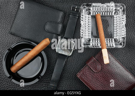 Due posacenere con i sigari, due portafogli e orologi da polso in pelle naturale, sullo sfondo di lusso Foto Stock