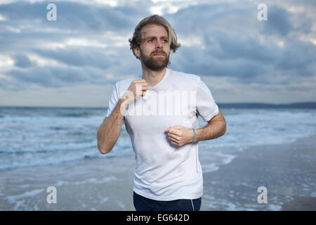 Un uomo nella sua 30's corre lungo una spiaggia con le nuvole scure sopra la testa Foto Stock