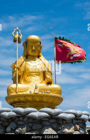 Golden Buddha seduto sul cuore piastrelle sagomate in possesso di una bandiera rossa con cielo blu Foto Stock