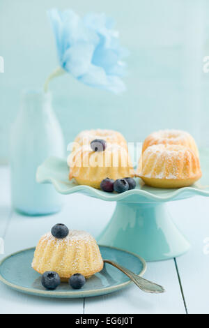 Mini bundt torte con lo zucchero a velo su una torta di stand con mirtilli e un fiore di carta Foto Stock