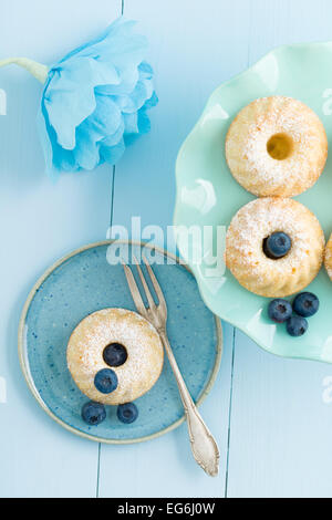 Mini bundt torte con lo zucchero a velo su una torta di stand con mirtilli e un fiore di carta Foto Stock