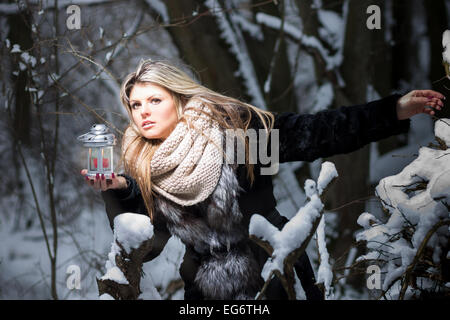 Favola invernale. Giovane donna nel bosco tenendo la luce di una candela guardando fuori Foto Stock