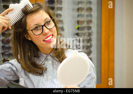 Giovani brunette cercando bicchieri rossi presso il negozio ottica con diverse cornici in background Foto Stock