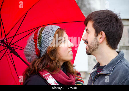 Ragazza caucasica e ragazzo lo scambio di sguardi amorevole sotto un ombrello rosso Foto Stock