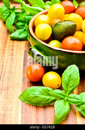 Una ciotola con pomodori e basilico foglie su un tavolo di legno Foto Stock