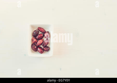 Rosa appassita hips in una ciotola su un tavolo bianco vista superiore Foto Stock