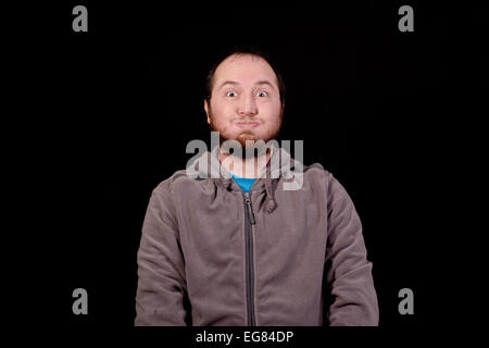 Giovane uomo che fa una faccia buffa isolato su nero Foto Stock