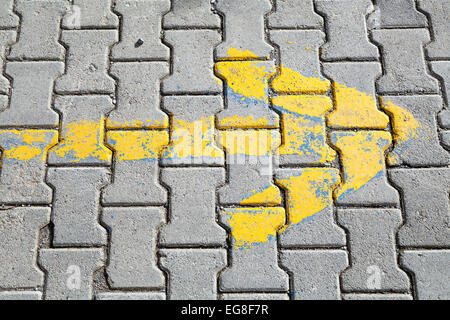 Una freccia gialla dipinta su grigio cobblestone pavement, direzione strada segno mostra modo giusto Foto Stock